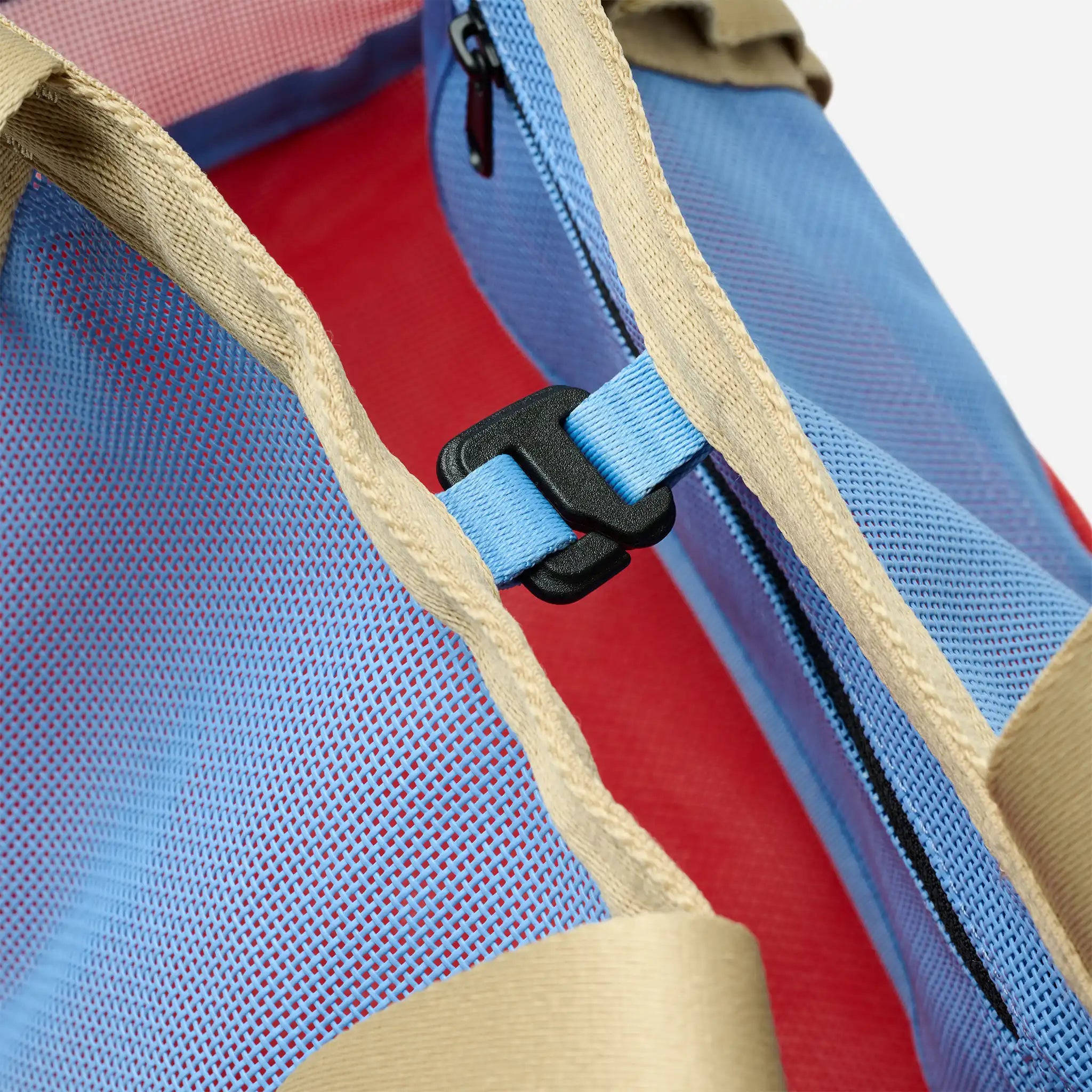Close-up of a backpack with blue and red interior, beige straps, and black zipper.