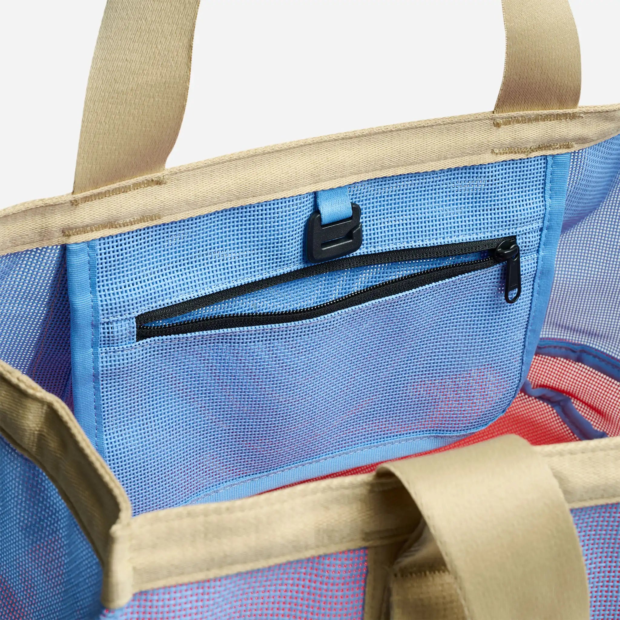 Close-up of a beige tote bag with a blue interior pocket and red lining.