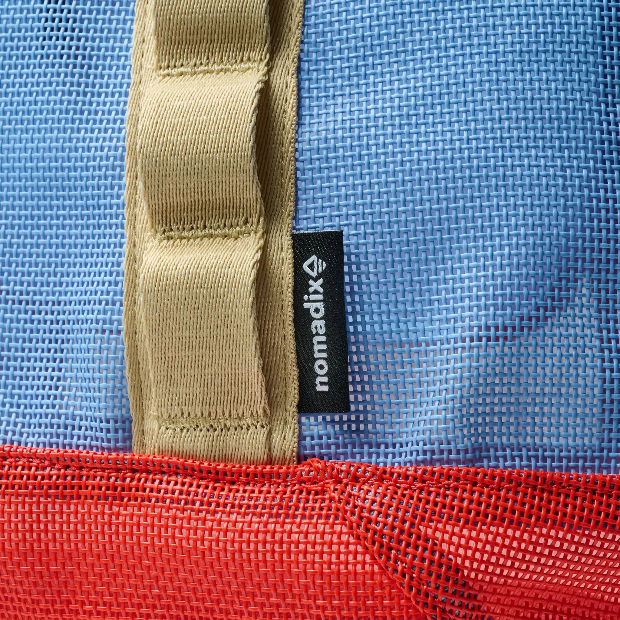 Close-up of a blue and red bag with a beige strap and a visible 'nomadix' label.