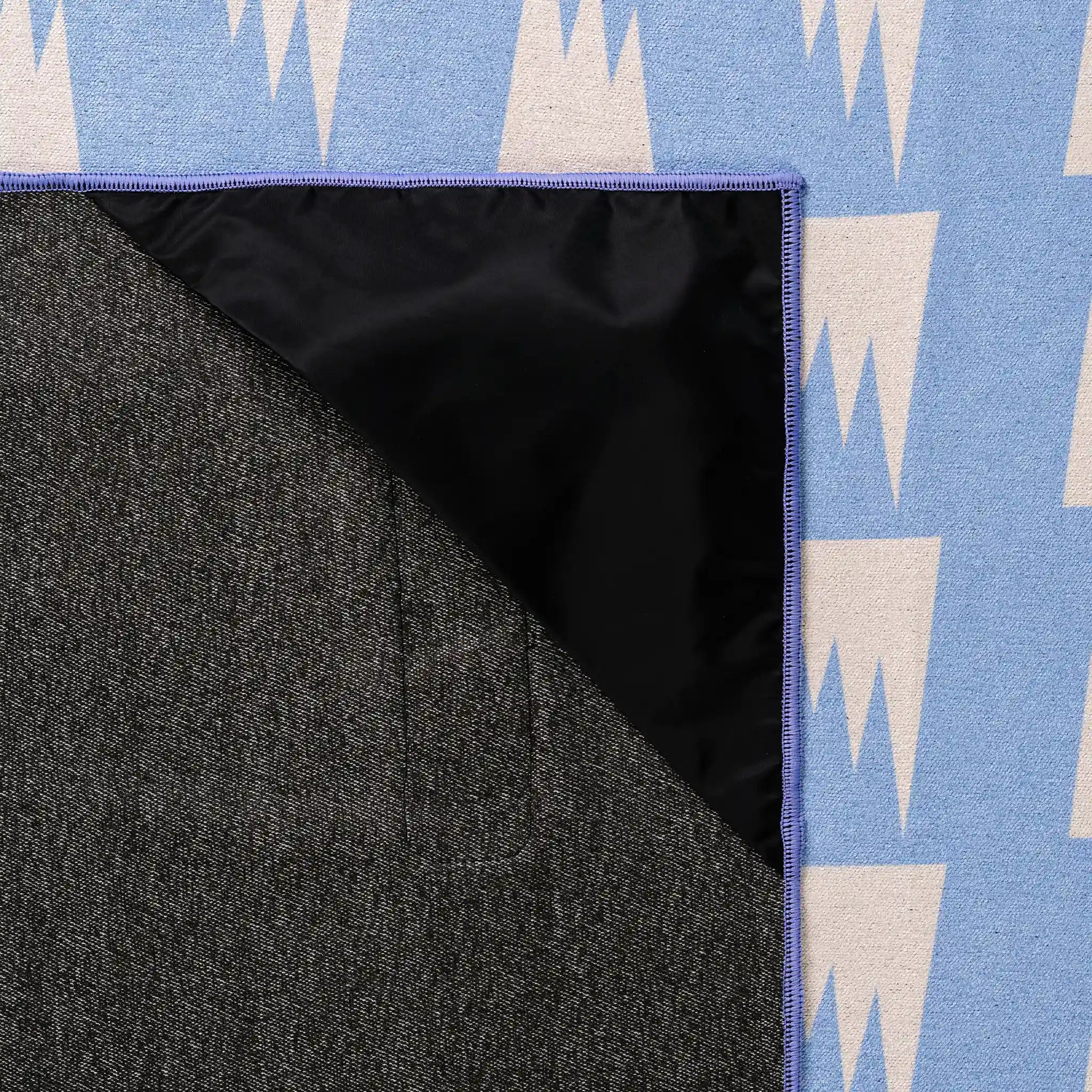 Close-up of a blue and white patterned rug with a black backing.