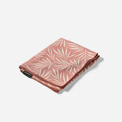 A folded pink blanket with a cream palm leaf pattern, shown on a light gray background.