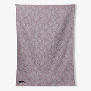 A rectangular fabric towel or blanket with an all-over palm leaf pattern in dusty mauve and white, featuring a small black 'hummus' brand tag in the bottom-left corner, shown against a plain light gray background.