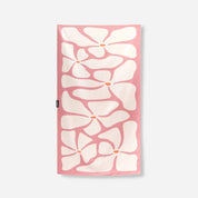 A rectangular pink towel featuring a bold white floral pattern with small orange centers, shown flat against a light gray background.