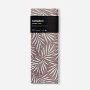 A packaged folded blanket towel by nomadix, featuring a brown and mint green palm leaf pattern with a black paper label at the top.