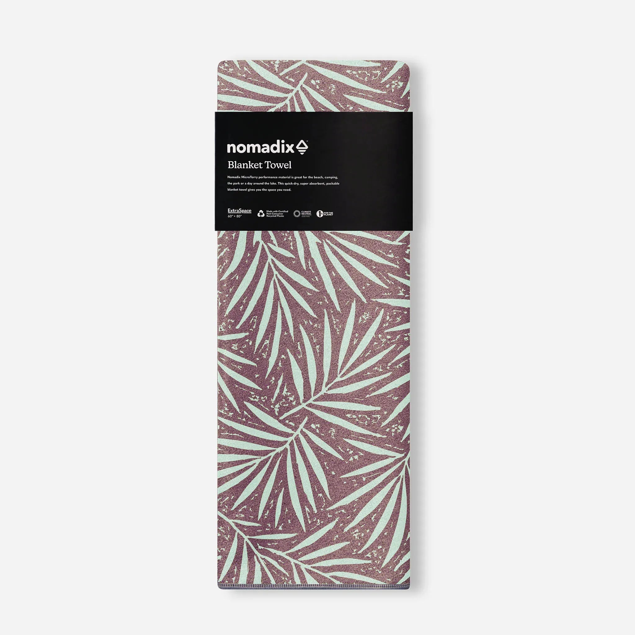 A packaged folded blanket towel by nomadix, featuring a brown and mint green palm leaf pattern with a black paper label at the top.