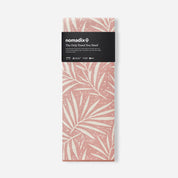 A folded Nomadix travel towel with a dusty pink and cream palm leaf pattern, wrapped in a black paper band with the brand logo.