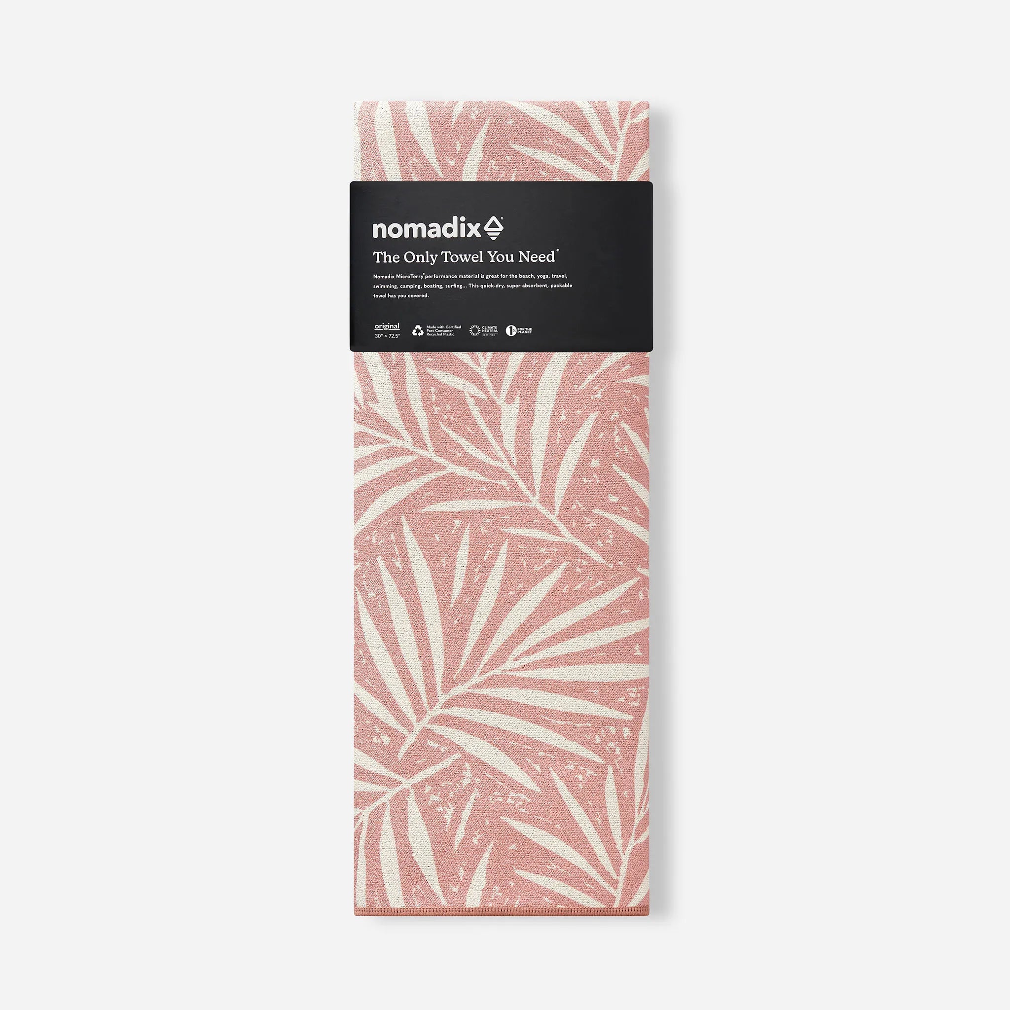 A folded Nomadix travel towel with a dusty pink and cream palm leaf pattern, wrapped in a black paper band with the brand logo.
