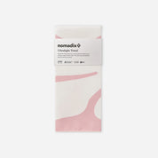 A folded white Nomadix ultralight towel with soft pink abstract wave patterns, wrapped in a white paper band labeled 'nomadix Ultralight Towel' on a light gray background.