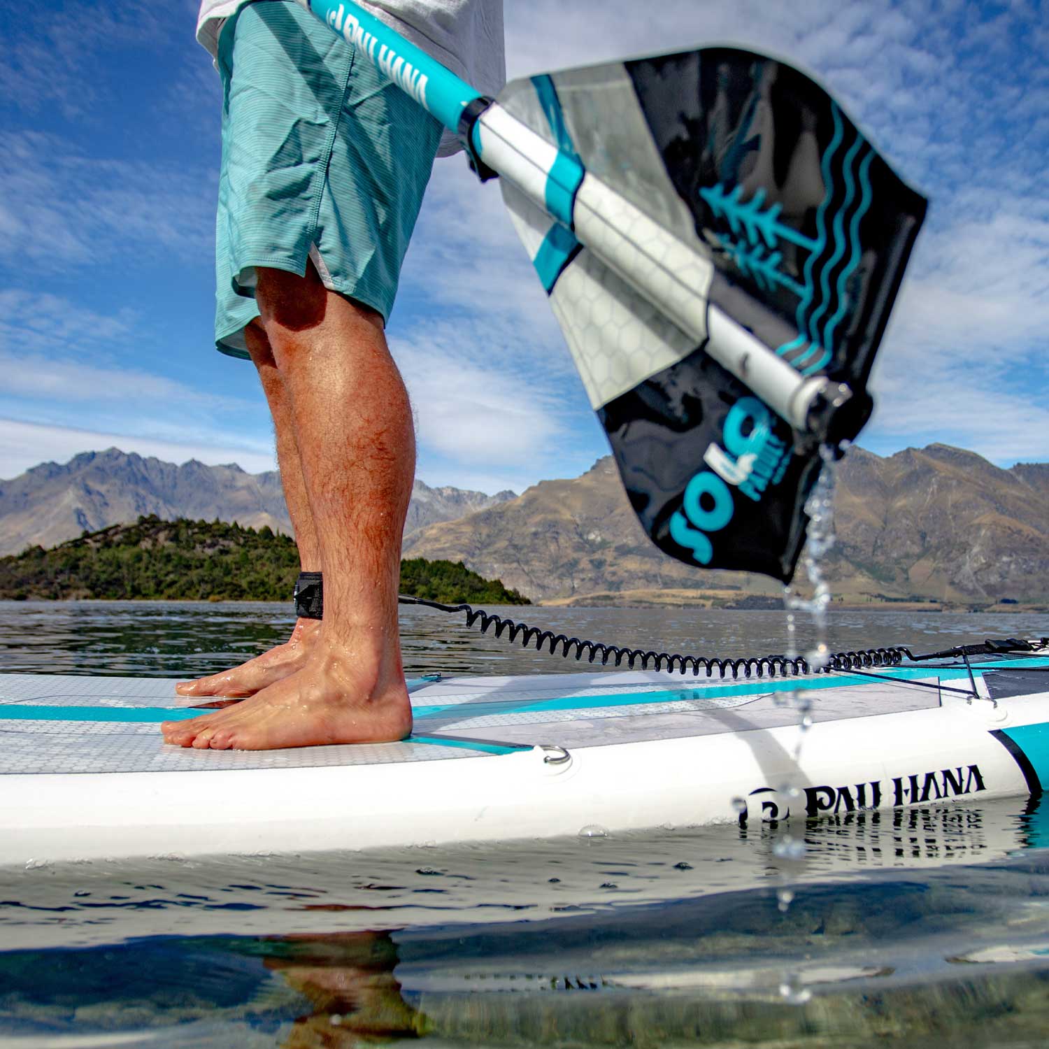 The Pau Hana Surf Supply Solo sup backcountry paddleboard paddle being lifted out the water showcasing textured  deck pad and safety leash