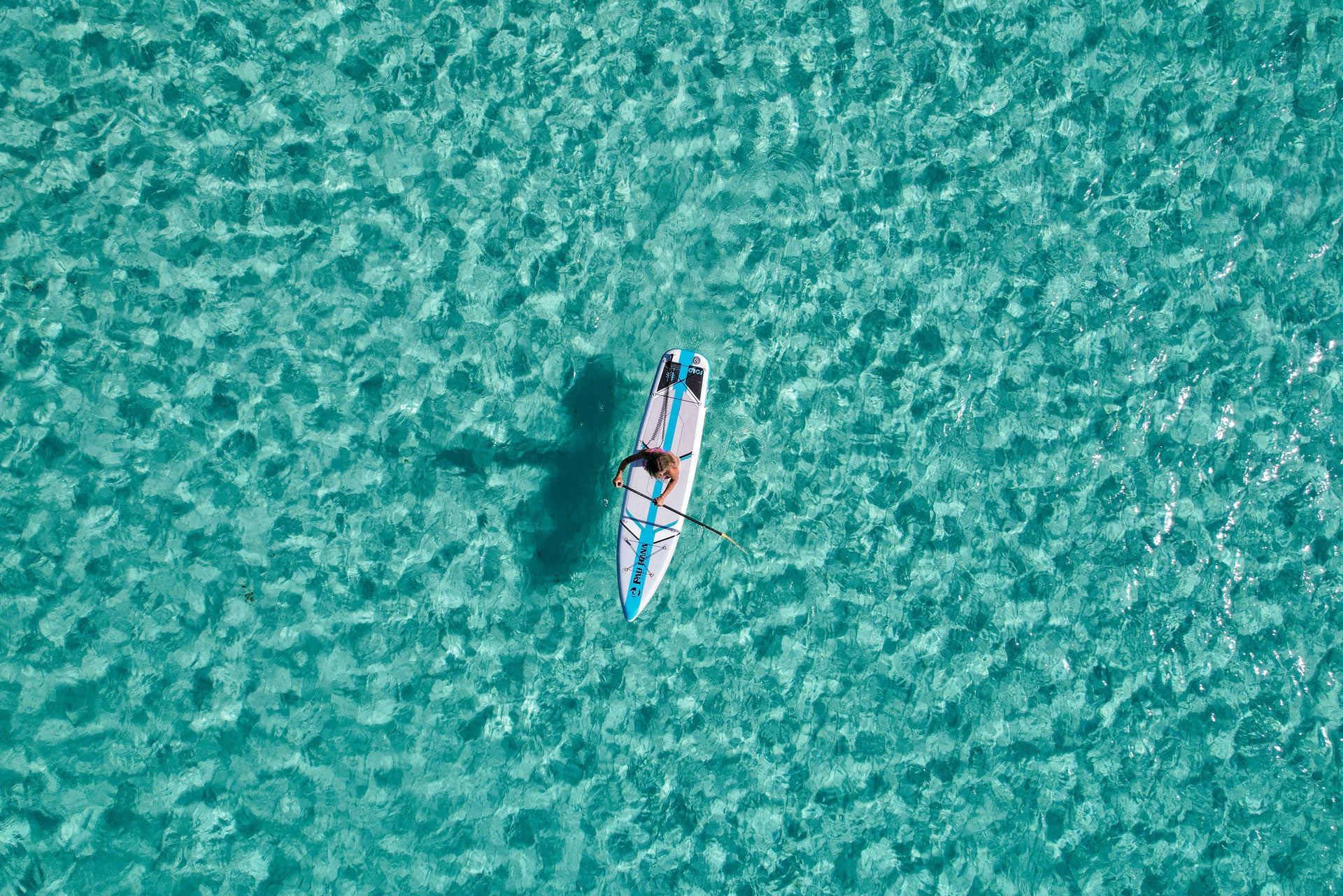 "Aerial drone shot of Pau Hana Surf Supply  Solo SUP backcountry board gliding through crystal-clear turquoise waters, showcasing stability and tracking performance"