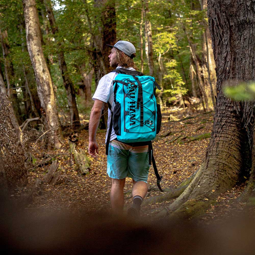 "Hiking through the woods wearing the Pau Hana Surf Supply Solo Sup Backcountry travel SUP in hiking backpack for remote lake access"