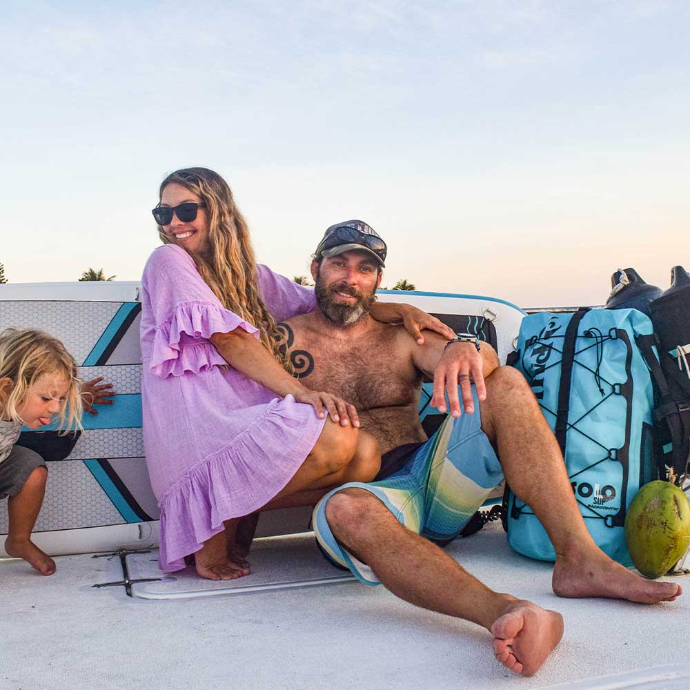 "Family relaxes on sailboat deck with Pau Hana Surf Supply Solo SUP backcountry board and coconut, capturing sunset adventure vibes"