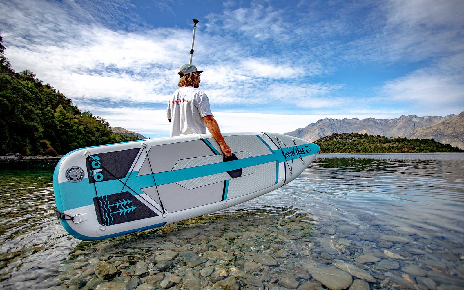 Pau Hana Surf Supply SOLO SUP in crystal-clear alpine lake, featuring seamount rigging system and teal wave graphics against mountain backdrop