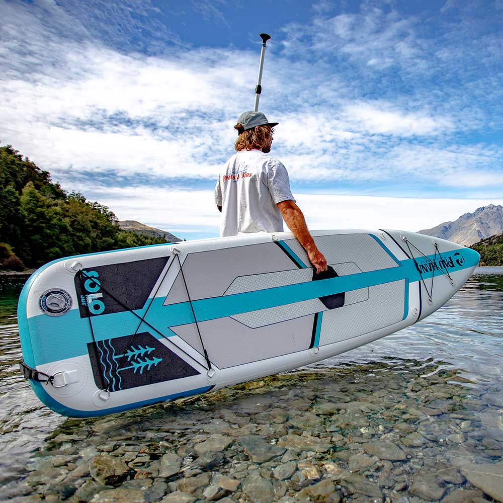 "Pau Hana Surf Supply Solo Backcountry SUP with fiberglass paddle explores crystal-clear alpine lake beneath mountains"