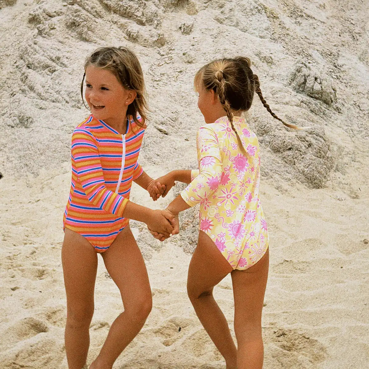 Two children in colorful swimsuits on a sandy beach.