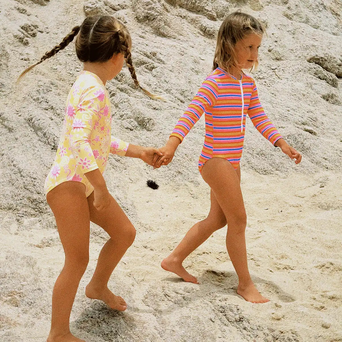 Two children in colorful swimsuits walking on a sandy beach.