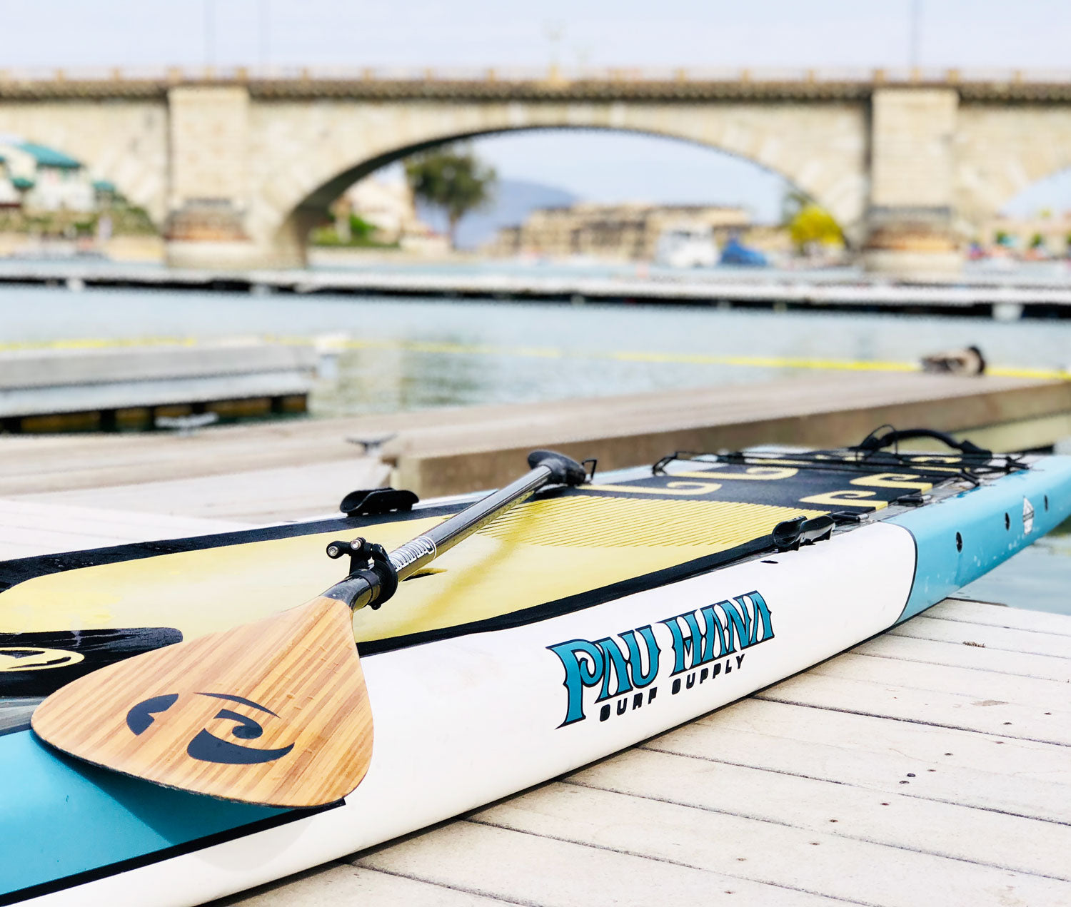 Paddleboard with a paddle on a dock with a bridge in the background