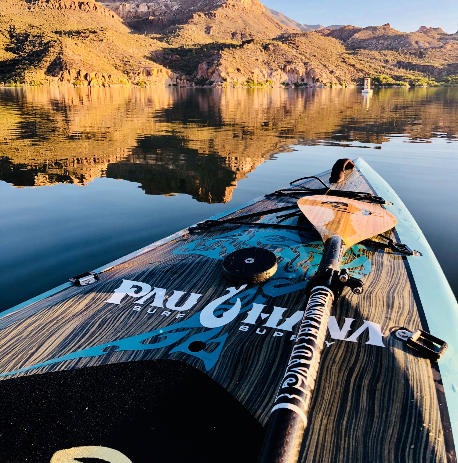 Paddleboard with a paddle on a calm lake with mountains in the background