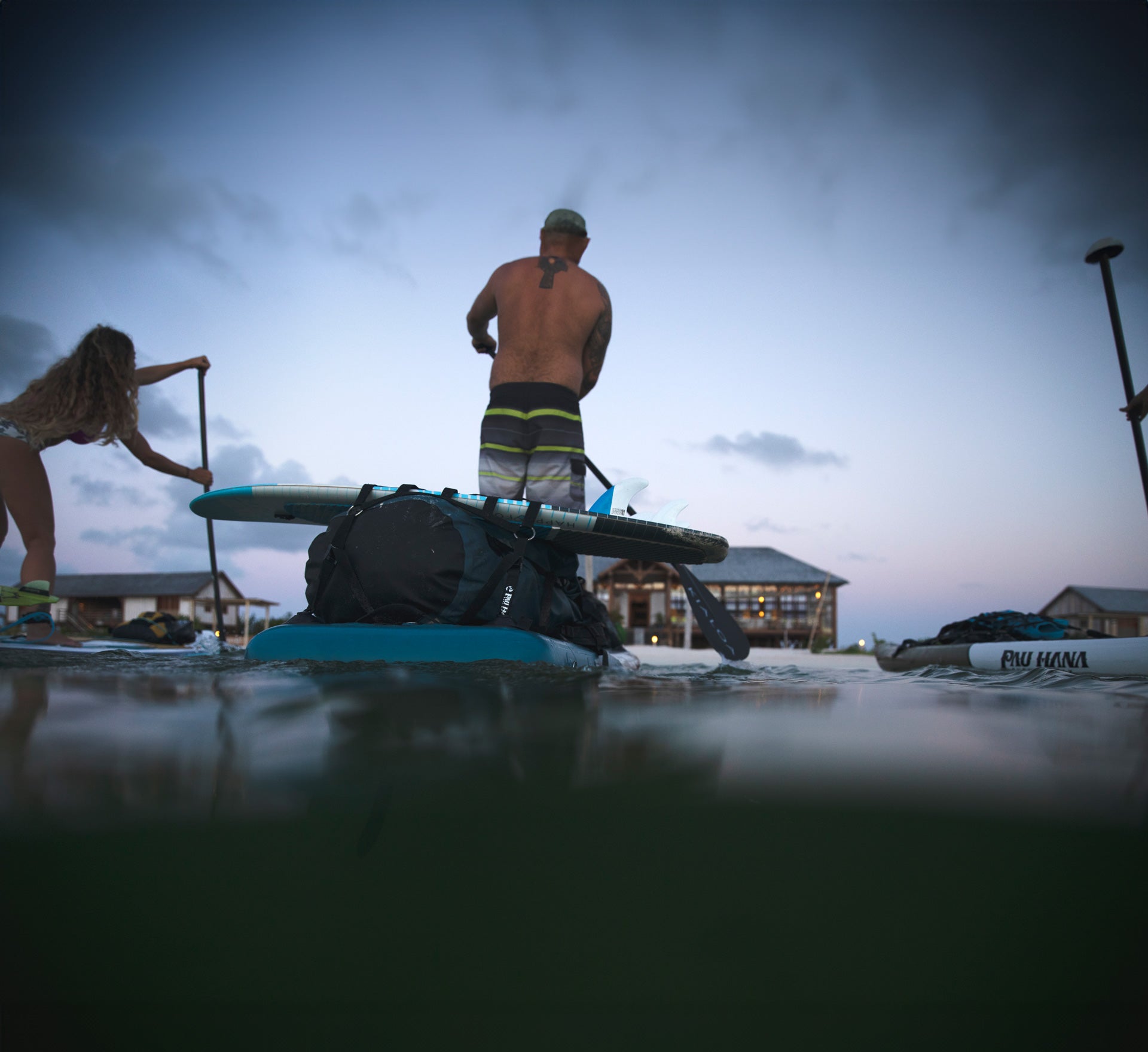 Paddleboarding at dusk in Barbuda past a resort with a loaded paddleboard with kiteboarding equipment on a Pau Hana Surf Supply 12&#39;0&quot; Endurance Air paddleboard