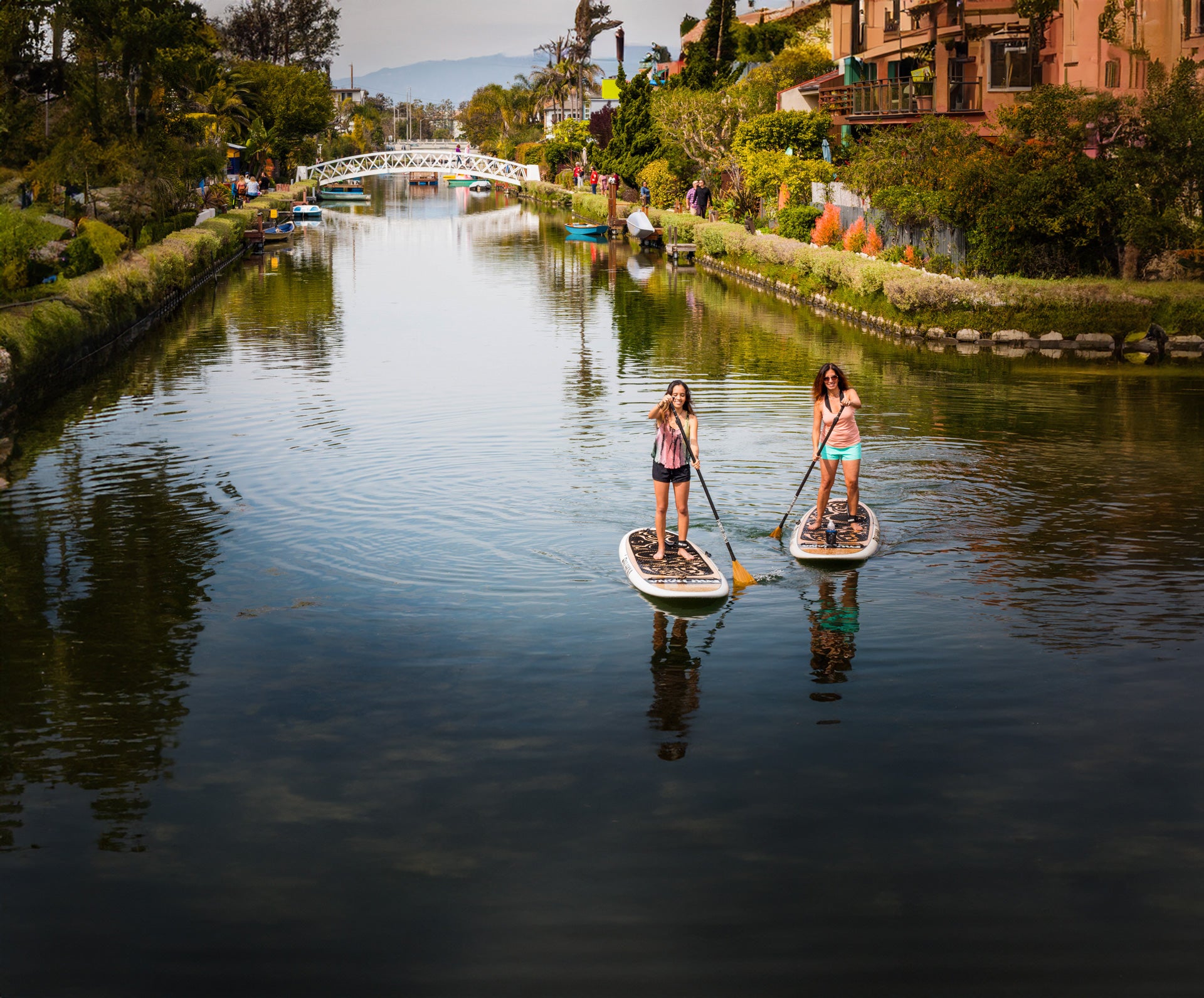 "Two paddlers cruising Venice Canal on the Pau Hana Surf Supply Oahu paddle board, white bridge backdrop"