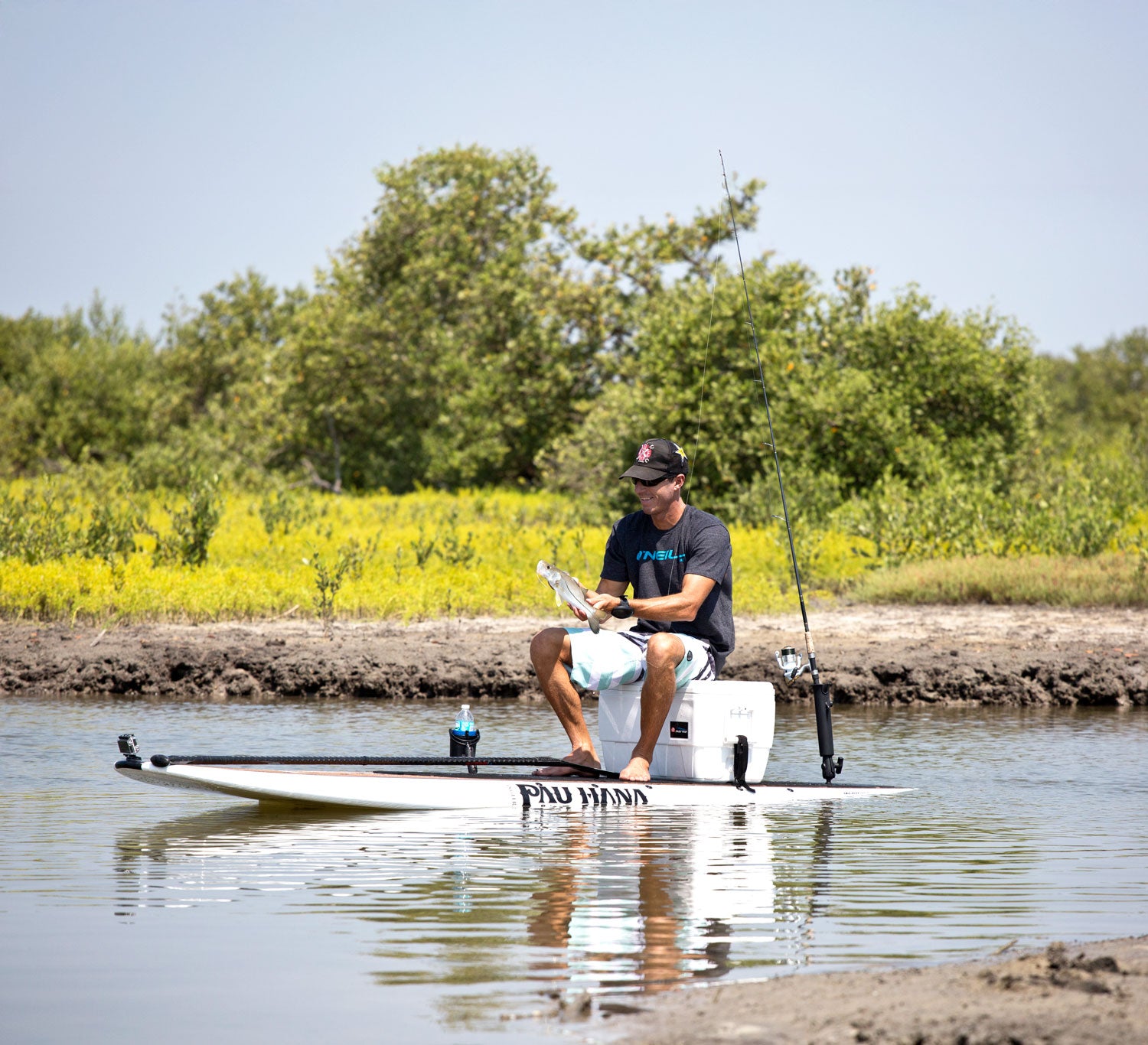 Man fishing from a paddleboard on a calm body of water with trees in the background