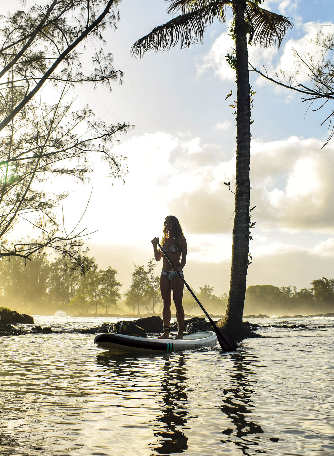 "Pau Hana Surf Supply Big EZ Air inflatable SUP at sunset along Hawaiian coastline, showcasing stability paddling near palm trees and lava rocks"