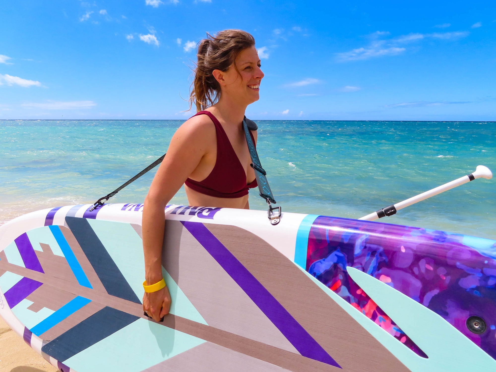 "Woman carrying a Pau Hana Surf Supply Moon Mist SUP with the Kamba Strap at Oahu beach, showcasing signature Cosmic Feather design and Moon Mist Paddle"