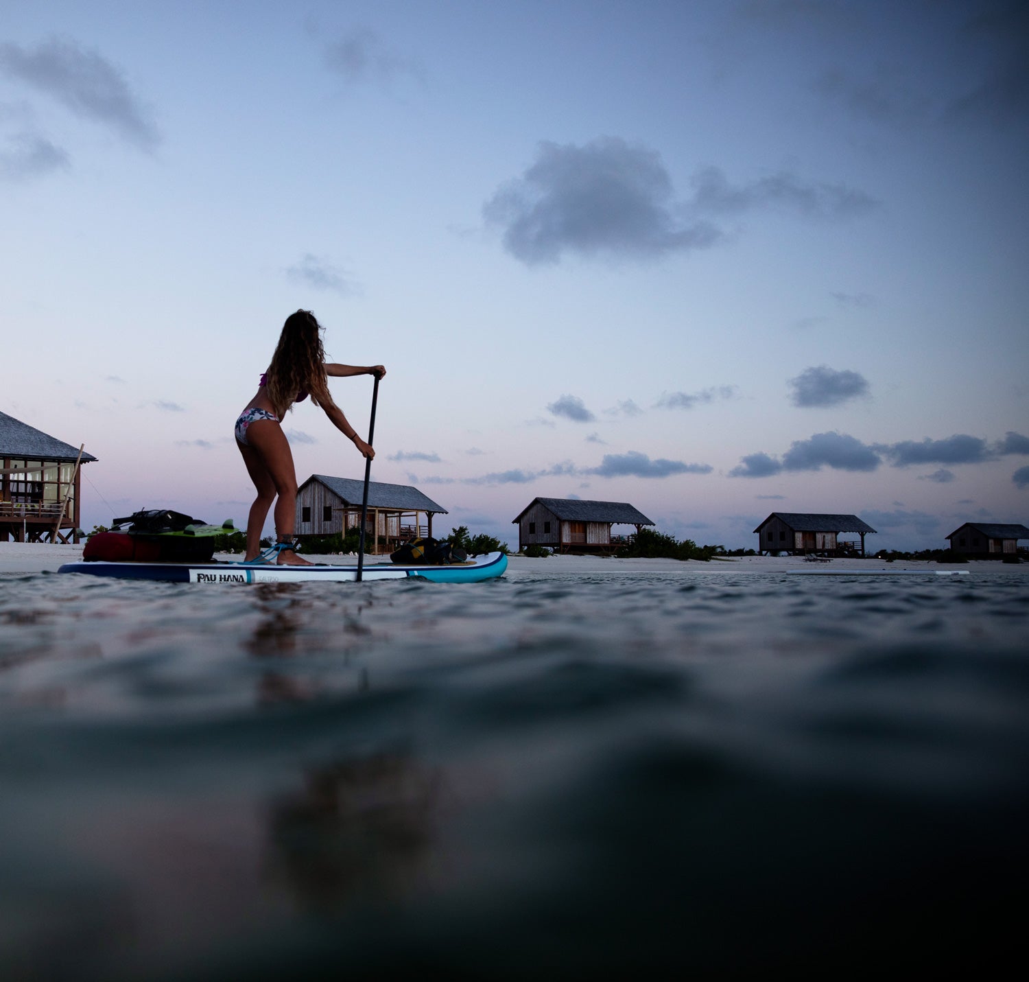 Paddleboarding at dusk in Barbuda past a resort with a loaded paddleboard with kiteboarding equipment on a Pau Hana Surf Supply Calypso Air keel hull inflatable paddleboard