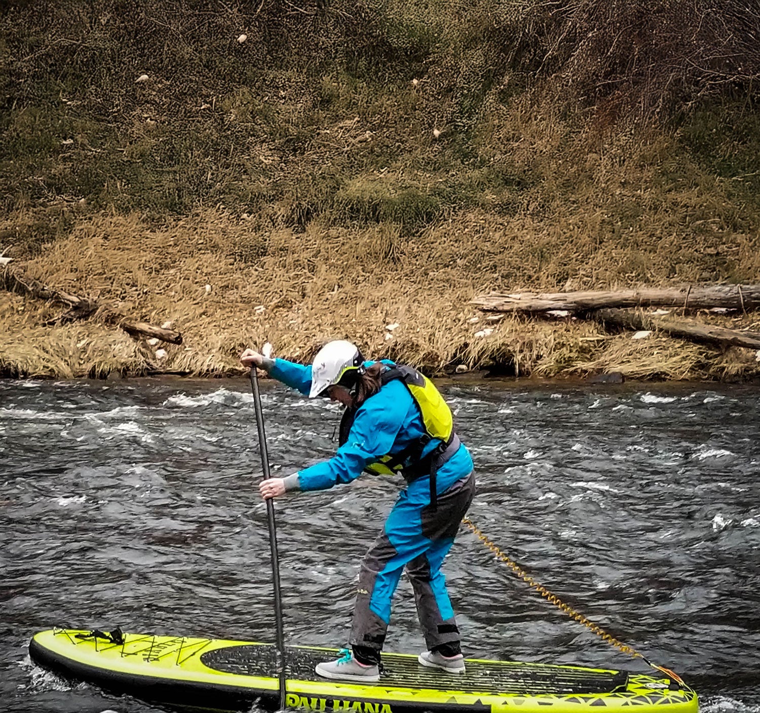 Person paddleboarding on a river with a grassy bank in the background