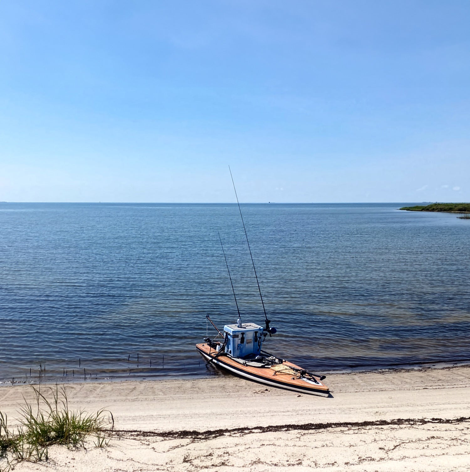 Paddleboard on a sandy beach with clear blue water and sky.
