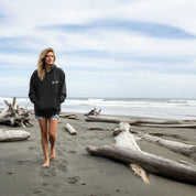 Woman walking on a beach with driftwood and ocean waves in the background