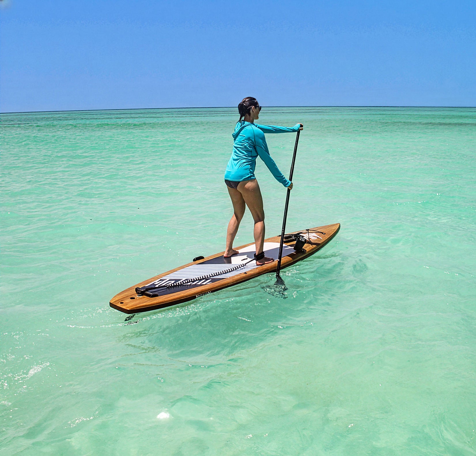 Person paddleboarding on clear turquoise water with a blue sky background