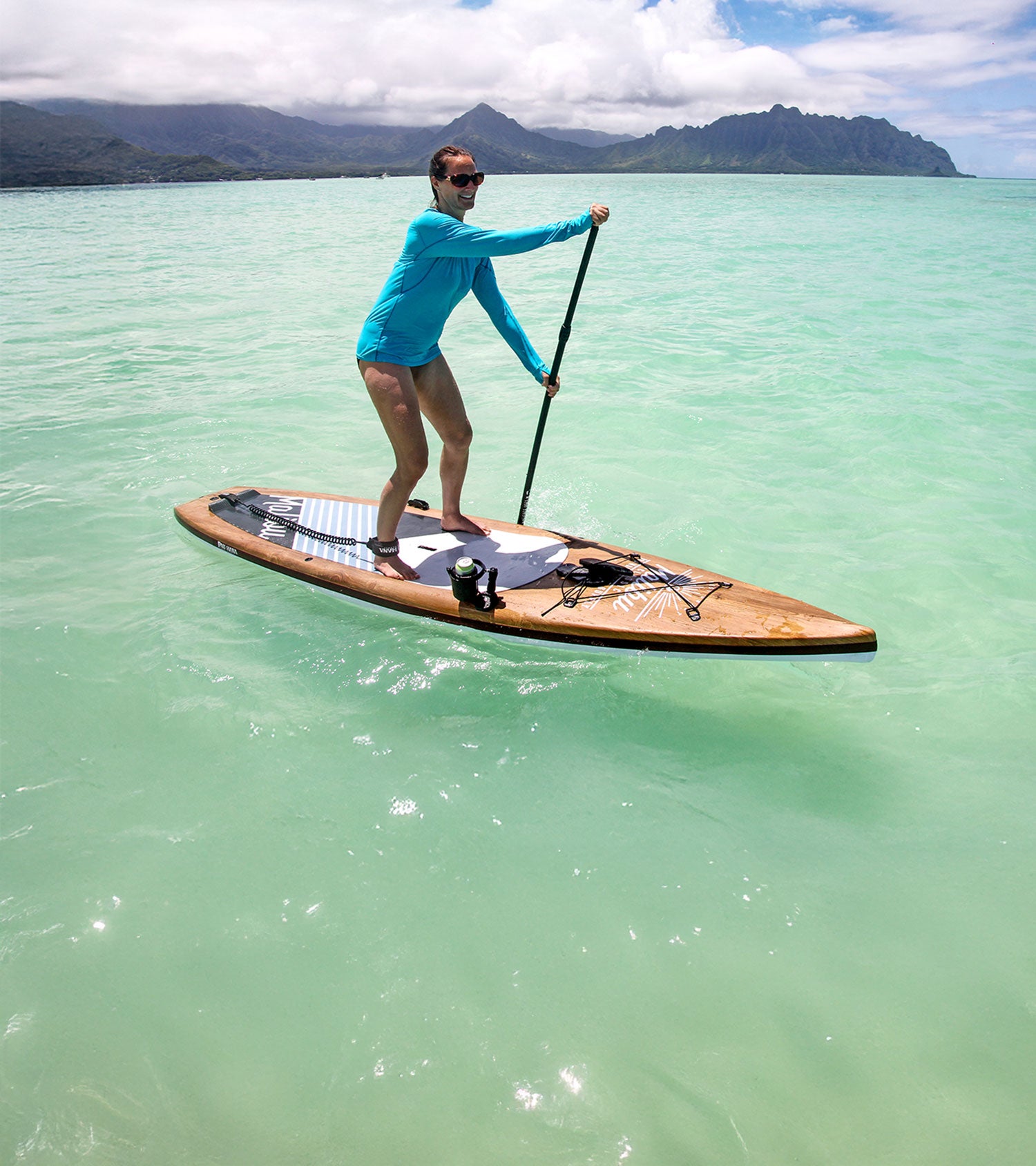 Person paddleboarding on clear green water with mountains in the background