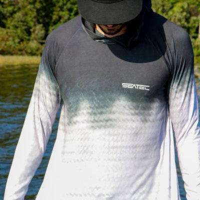 Person wearing a gray and white gradient long-sleeve shirt with 'Seatec' branding outdoors.