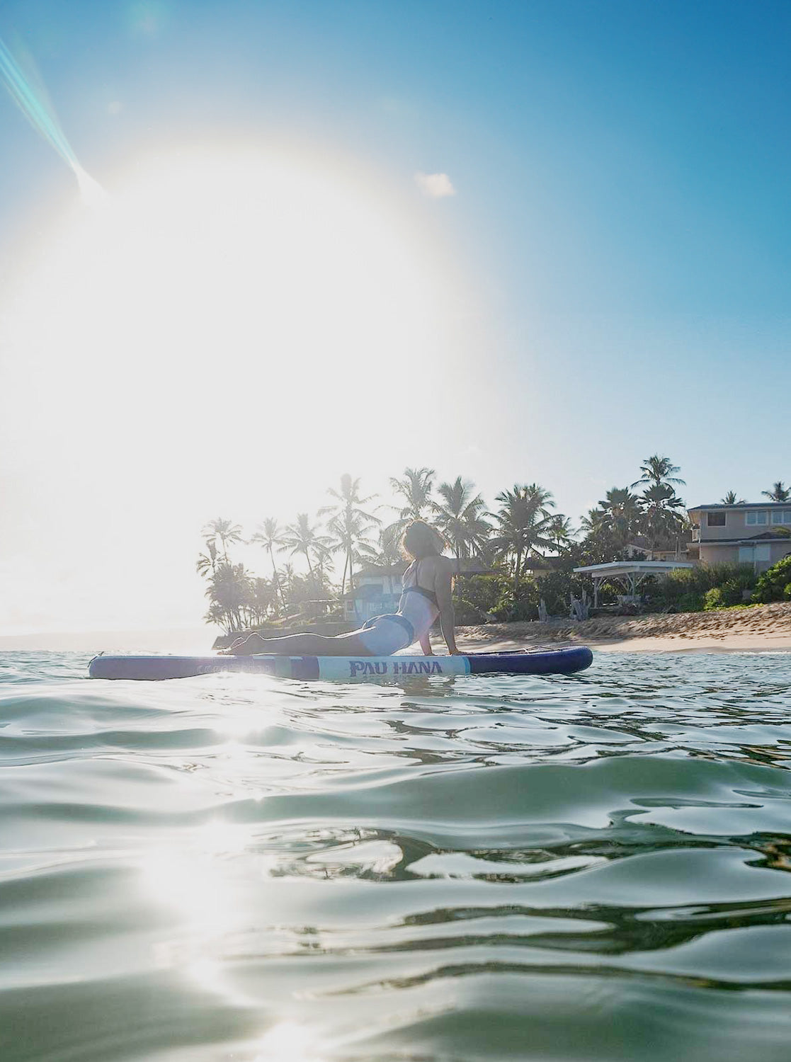 "Pau Hana Surf Supply Moon Mist TPU yoga board action shot - practitioner in cobra pose with tropical Hawaiian sunset backdrop, palms silhouetted"