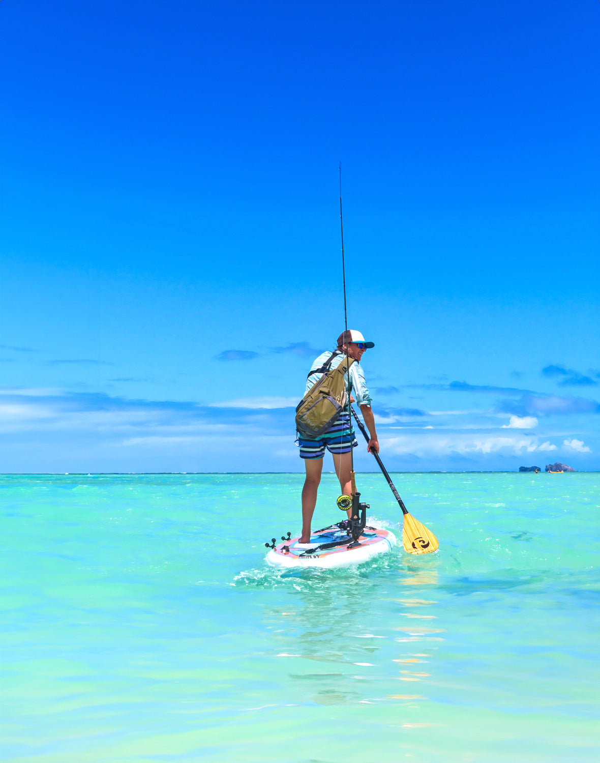 "Pau Hana Surf Supply Navio Keel Hull SUP board rigged for fly fishing in crystal-clear Hawaiian waters with standing angler and carbon teak paddle"