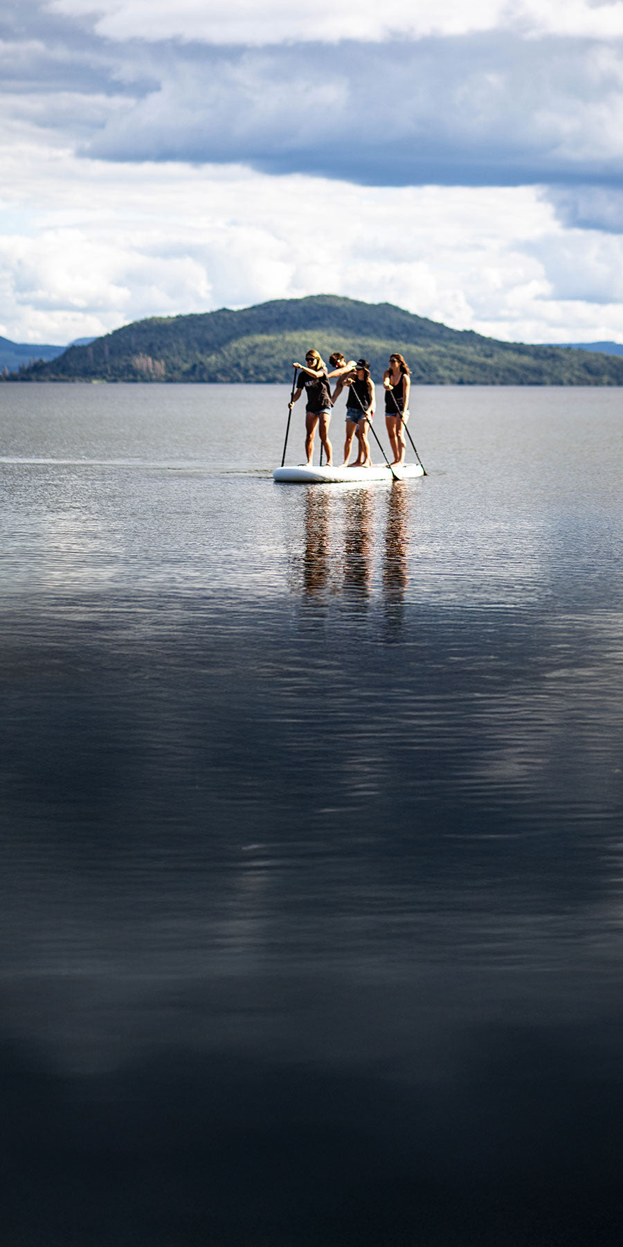 Group of people on a stand-up paddleboard in a calm lake with mountains in the background