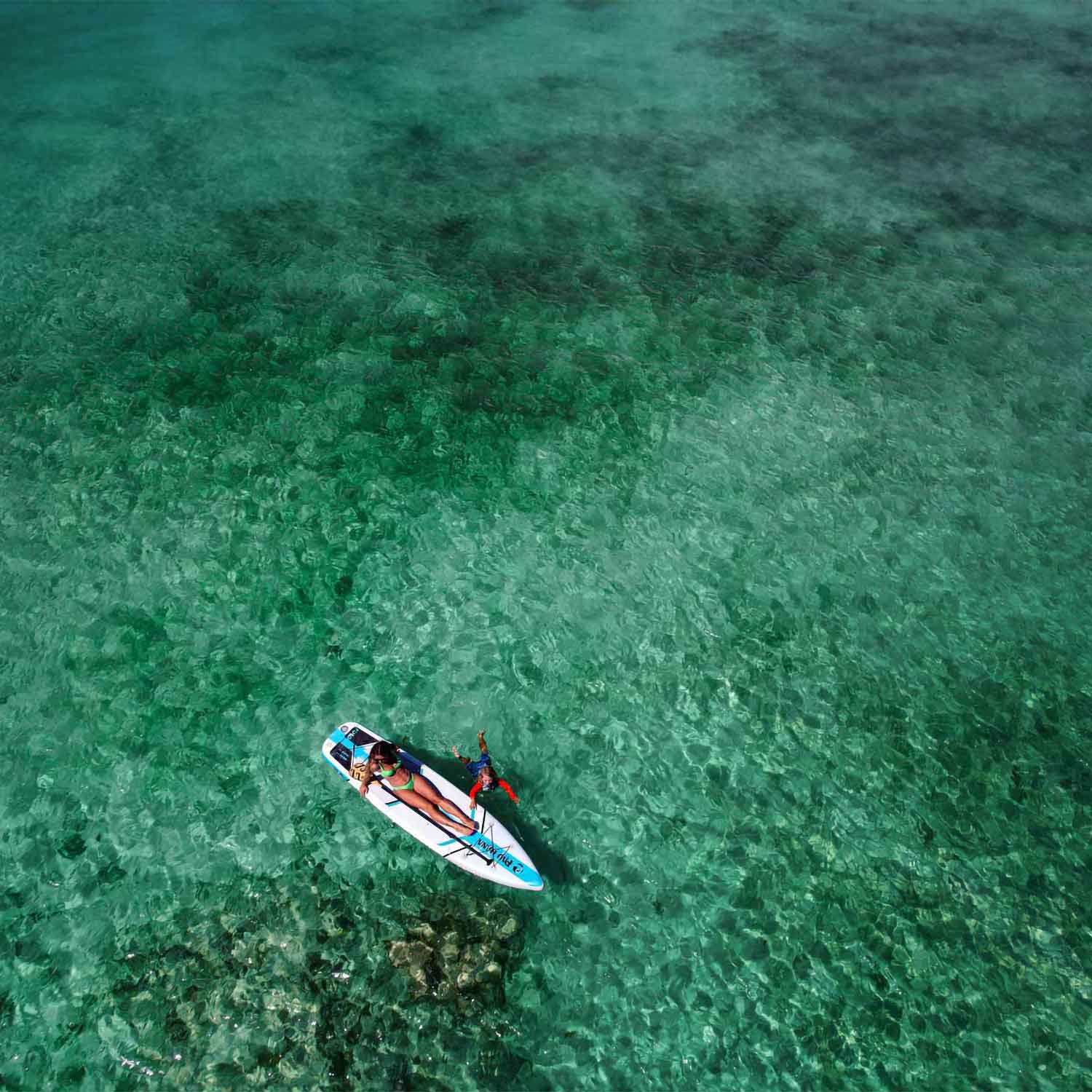 an aerial image of a woman and child on the solo sup backcountry paddleboard on the ocean