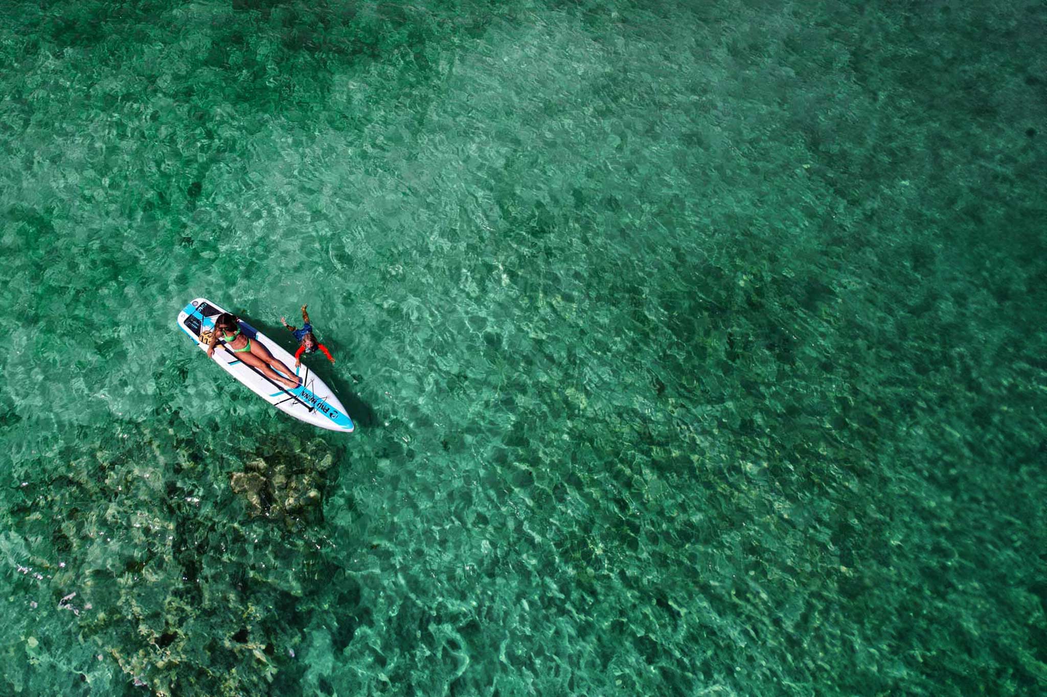 an aerial image a woman and child on the solo sup backcountry paddleboard on right turquise water. 