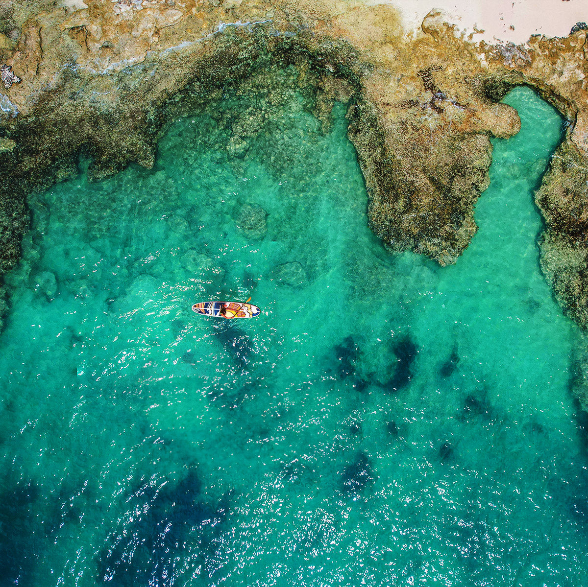 "Pau Hana Surf Supply SUP exploring emerald lagoon - aerial shot showcasing tidal reef pools and Stowaway Lite inflatable board with hippy wave design"